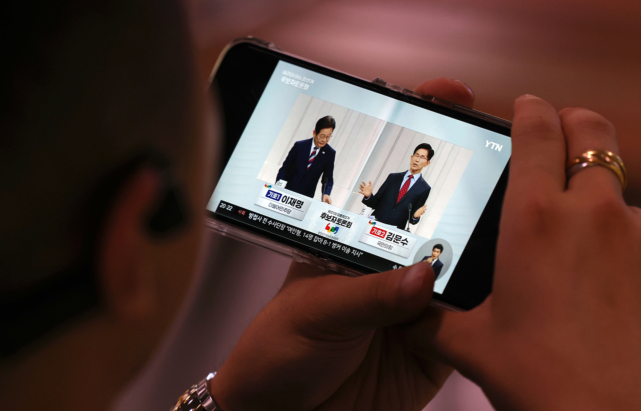 A viewer watches Democratic Party of Korea candidate Lee Jae-myung and People Power Party candidate Kim Moon-soo take part in a televised presidential debate on a smartphone on Tuesday. (Newsis)