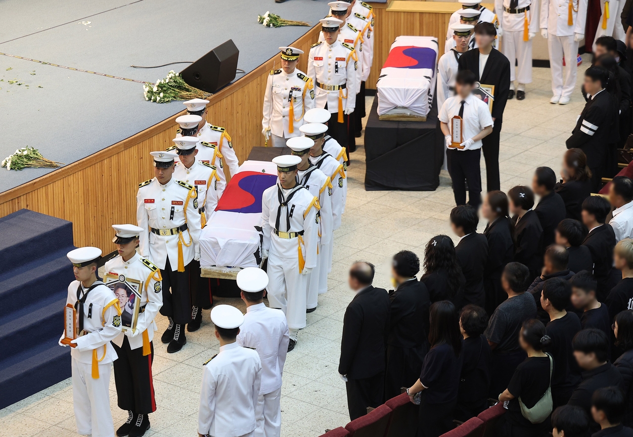 Navy honor guards carry the flag-draped caskets of four fallen officers during a memorial service held Sunday at the Naval Air Command auditorium in Pohang, North Gyeongsang Province. (Yonhap)