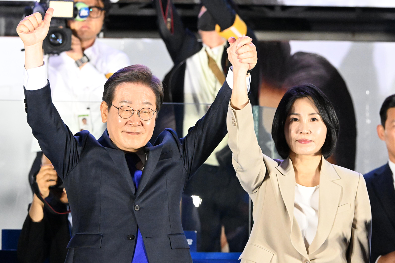 Lee Jae-myung (left) and his wife Kim Hye-kyung greet supporters as broadcasters called the election for Lee, early Wednesday morning. (Pool photo via Yonhap)