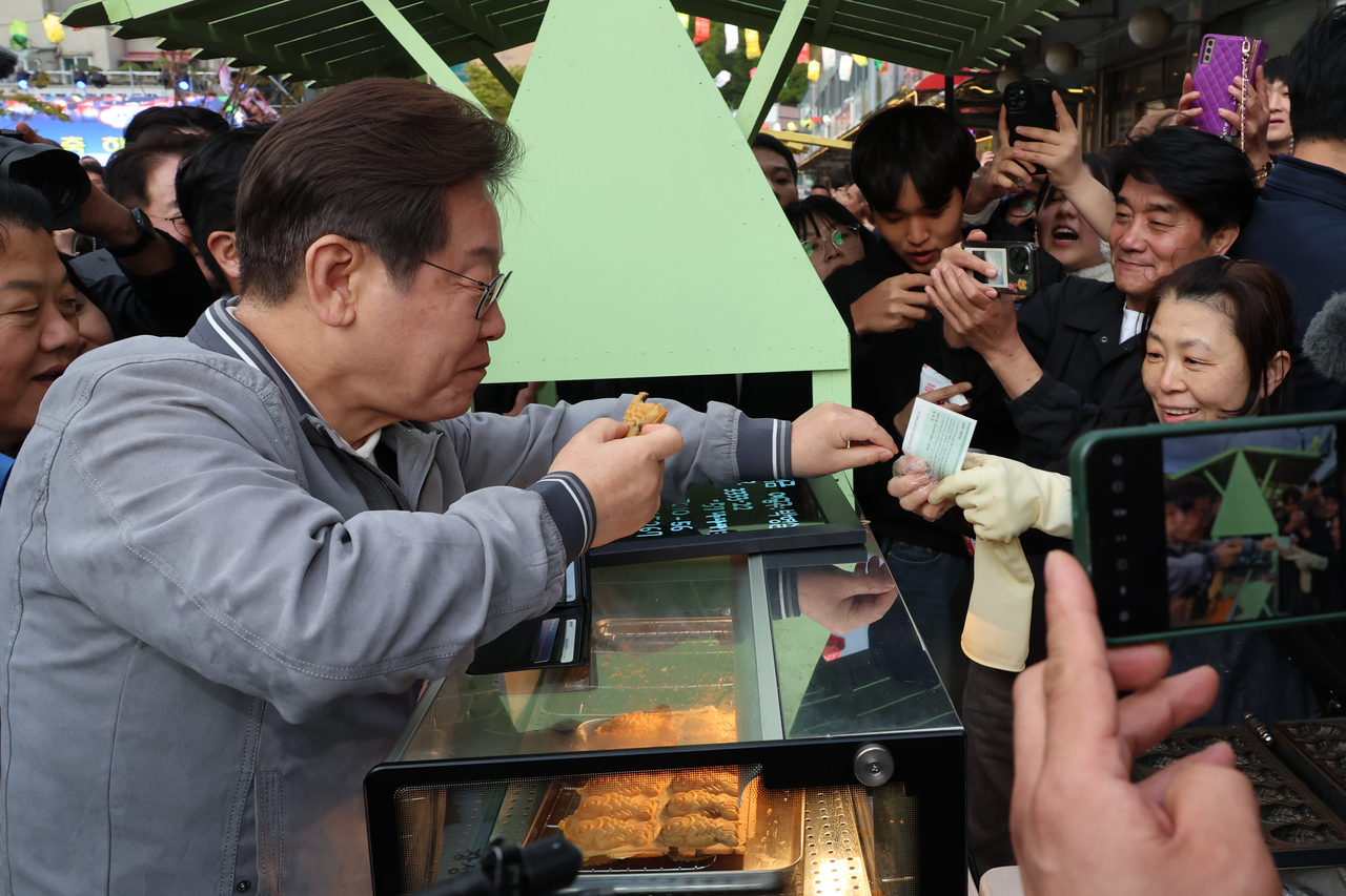 이재명 대통령이 지난달 3일 대선 후보 시절 강원 태백시 장성동 산나물 축제장에서 붕어빵을 사먹으며 호빵맨토토를 사용하고 있는 모습. [연합]