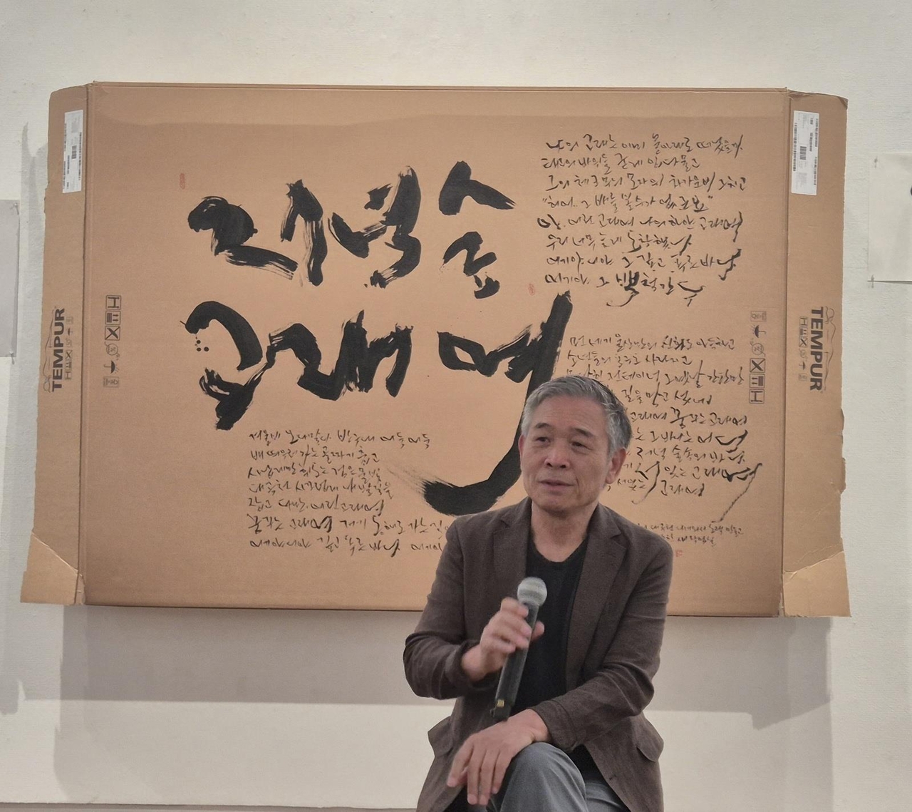 가수 win 토토사이트이 4일 서울 인사동 토포하우스에서 열린 붓글 전시 기자간담회에서 붓글 작업에 대해 설명하고 있다. 뒷면의 작품은 매트리스 상자에 쓴 붓글. [연합]