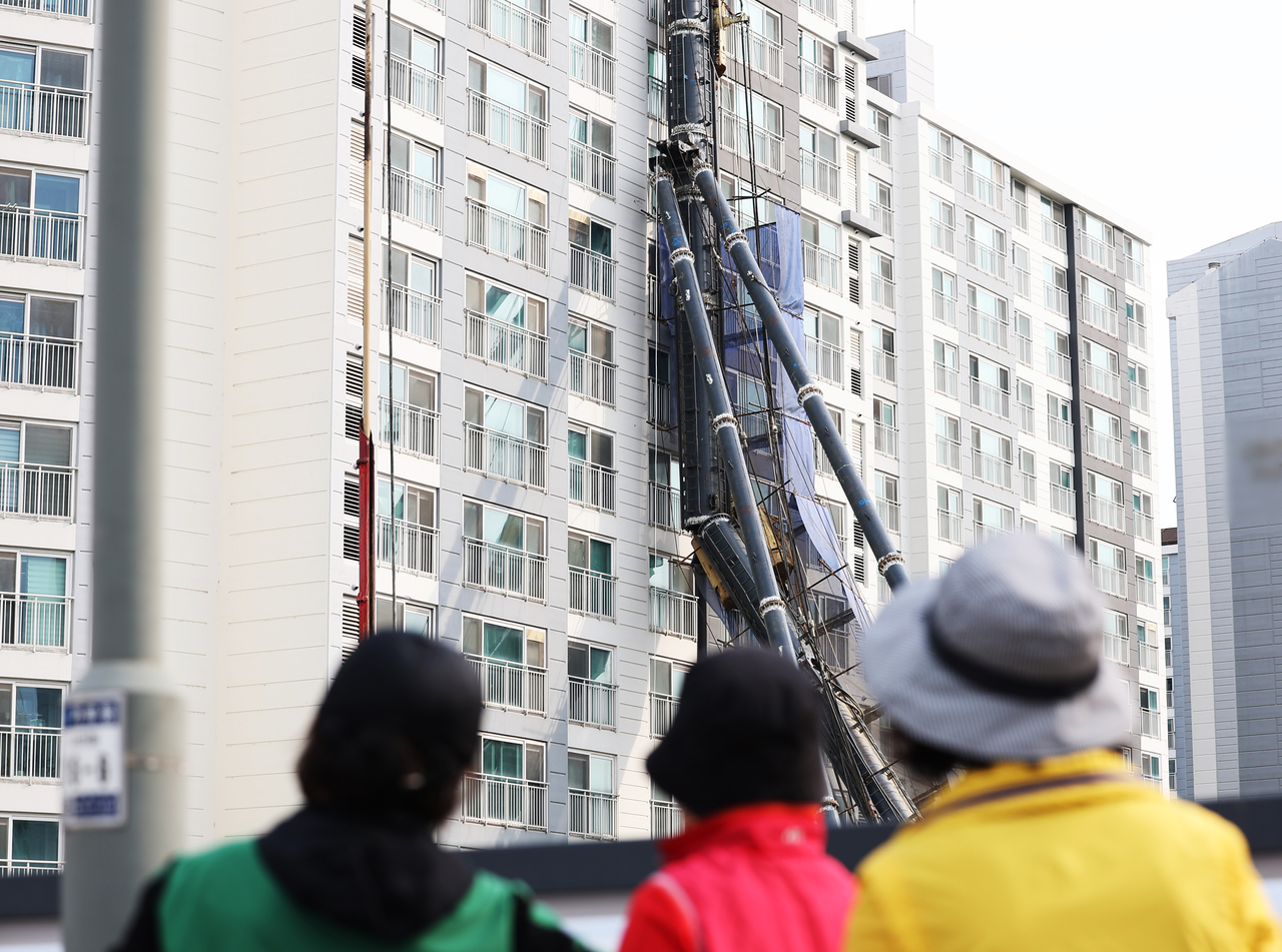 People look at the 80-ton drilling rig that tipped over Thursday night and is currently leaning against the walls of an apartment building on Friday, in Yongin, Gyeonggi Province. (Yonhap)