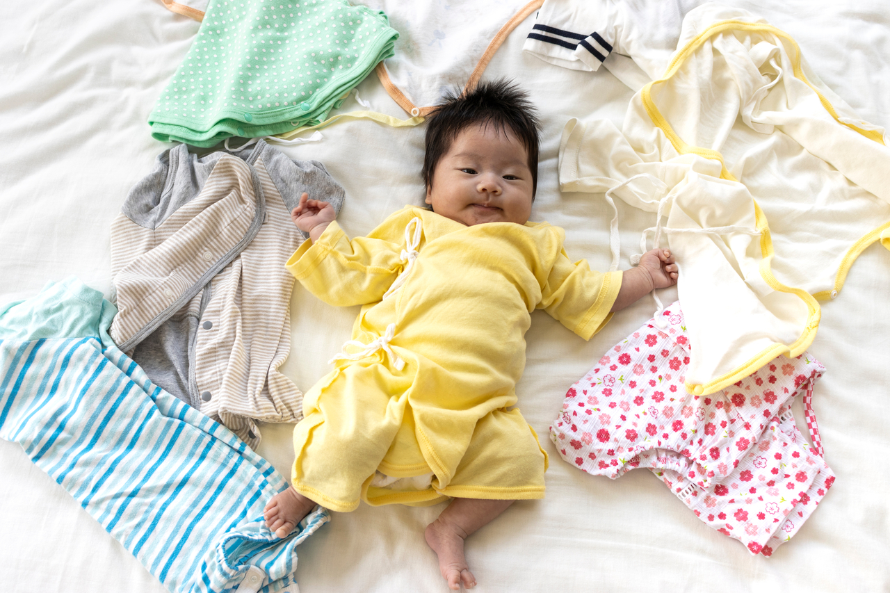 A baby is surrounded by lots of clothes. (123rf)