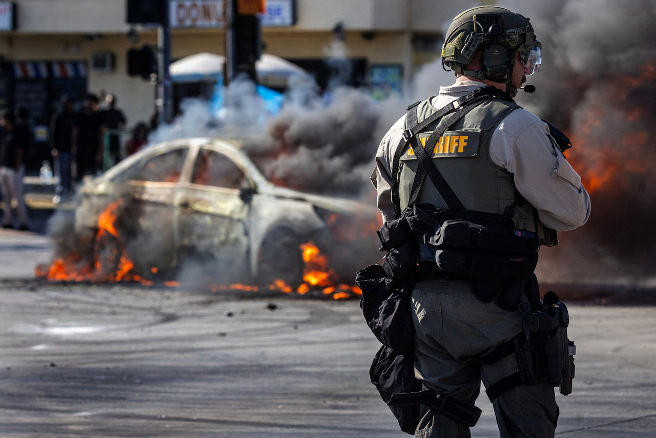 Smoke rises from a burning car on Atlantic Boulevard, during a standoff by protesters and law enforcement, following multiple detentions by Immigration and Customs Enforcement, in the Los Angeles County city of Paramount, California, Saturday.   Reuters-Yonhap