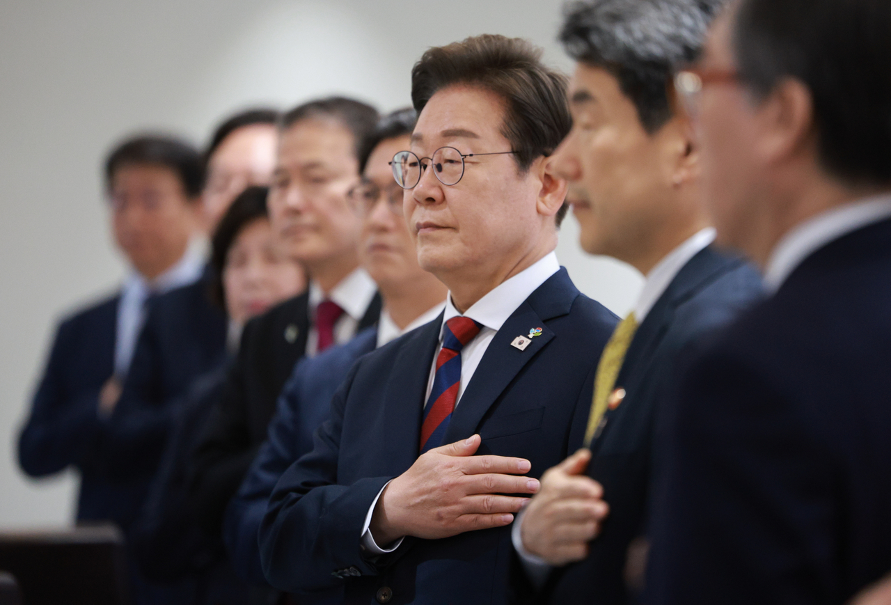 President Lee Jae-myung (third from right) stands with his hand over his heart as looks to the national flag, alongside members of his Cabinet who were nominated by former President Yoon Suk Yeol (not in the photo), including Deputy Prime Minister Lee Ju-ho (second from right) during a Cabinet meeting at the presidential office in Seoul on Thursday. (Pool photo via Yonhap)