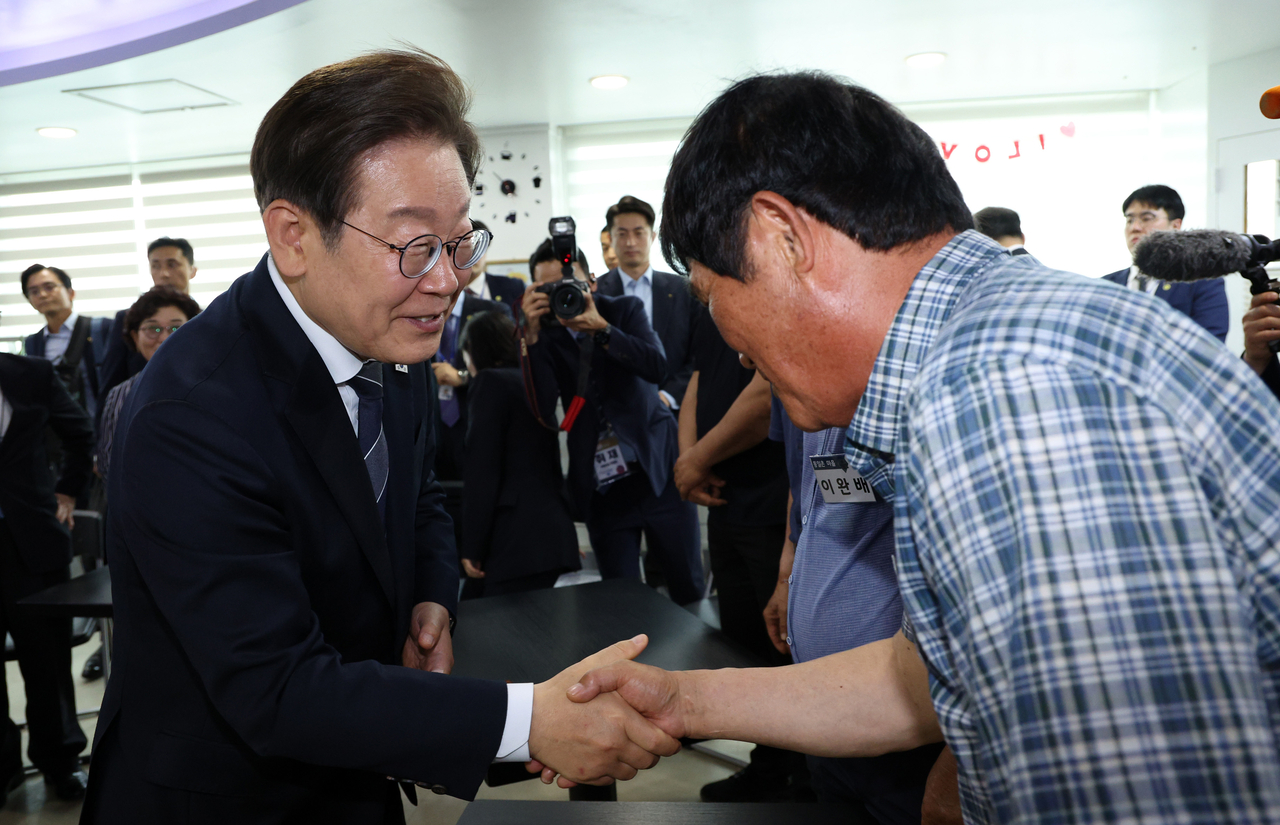 President Lee Jae-myung (left) shakes hands with a resident in Jangdan-myeon, Paju, Gyeonggi Province, on Friday. (Pool photo via Yonhap)