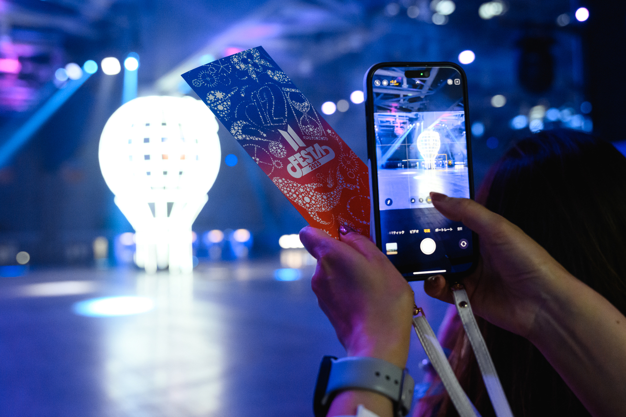 A fan photographs a balloon-shaped light installation at "Army Bomb Photo Spot" while holding a 2025 BTS Festa ticket at Kintex in Goyang, Gyeonggi Province, Friday. (Big Hit Music)