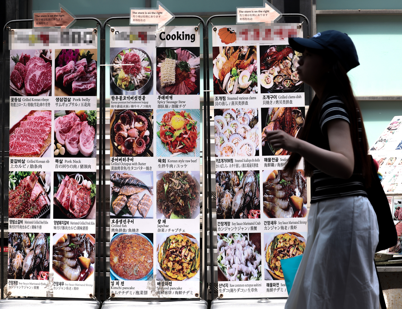 A woman passes by signs showing dishes at a restaurant in Myeong-dong, central Seoul, on Sunday. Yonhap