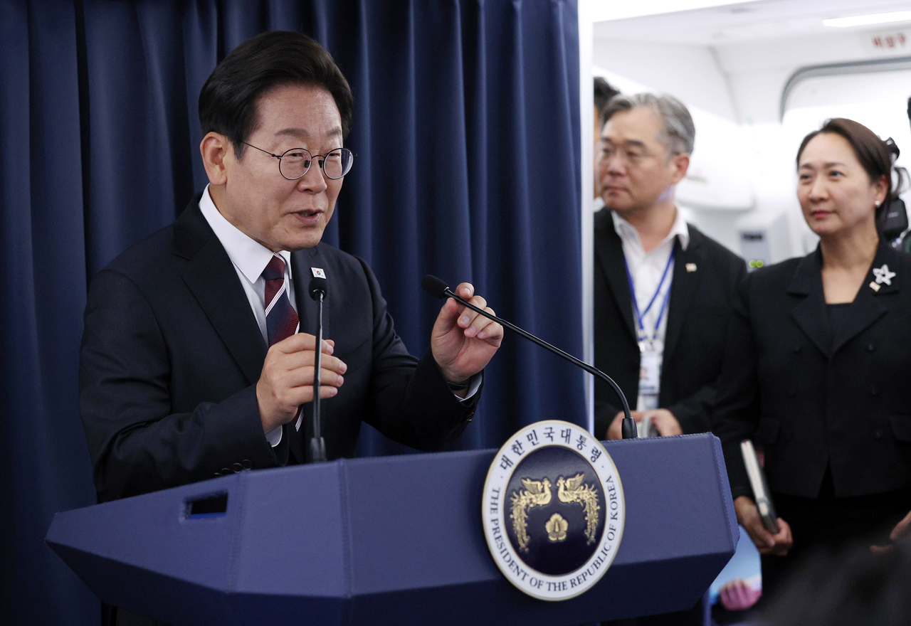 President Lee Jae-myung (left) speaks during a news conference while aboard Air Force One bound for Canada Monday. (Yonhap)