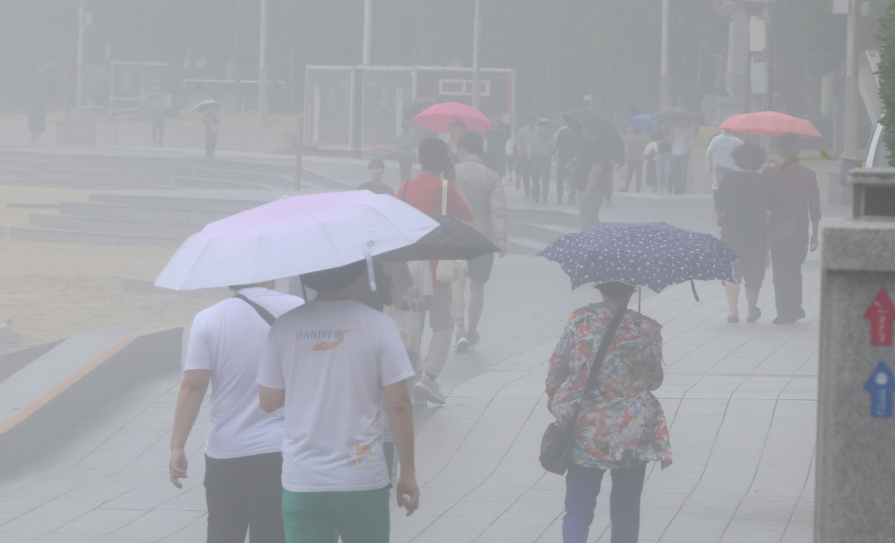 People walk with umbrellas near Haeundae Beach in Busan, which is shrouded in heavy fog and rain on Friday. (Yonhap)