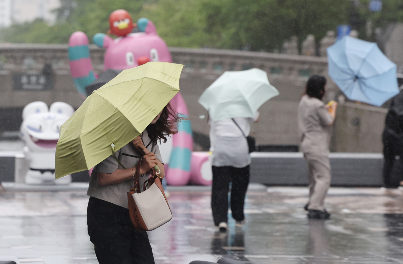 People holding umbrellas walk along Cheonggye Stream in downtown Seoul through wind and rain on Friday. (Yonhap)
