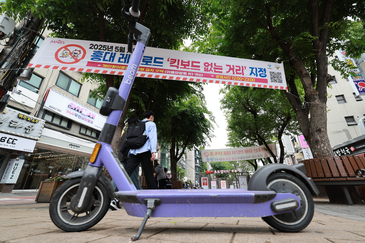 An e-scooter is seen in a street of Hongdae, Seoul’s Mapo District, below a banner announcing the area's designation as a no-scooter zone. (Yonhap)