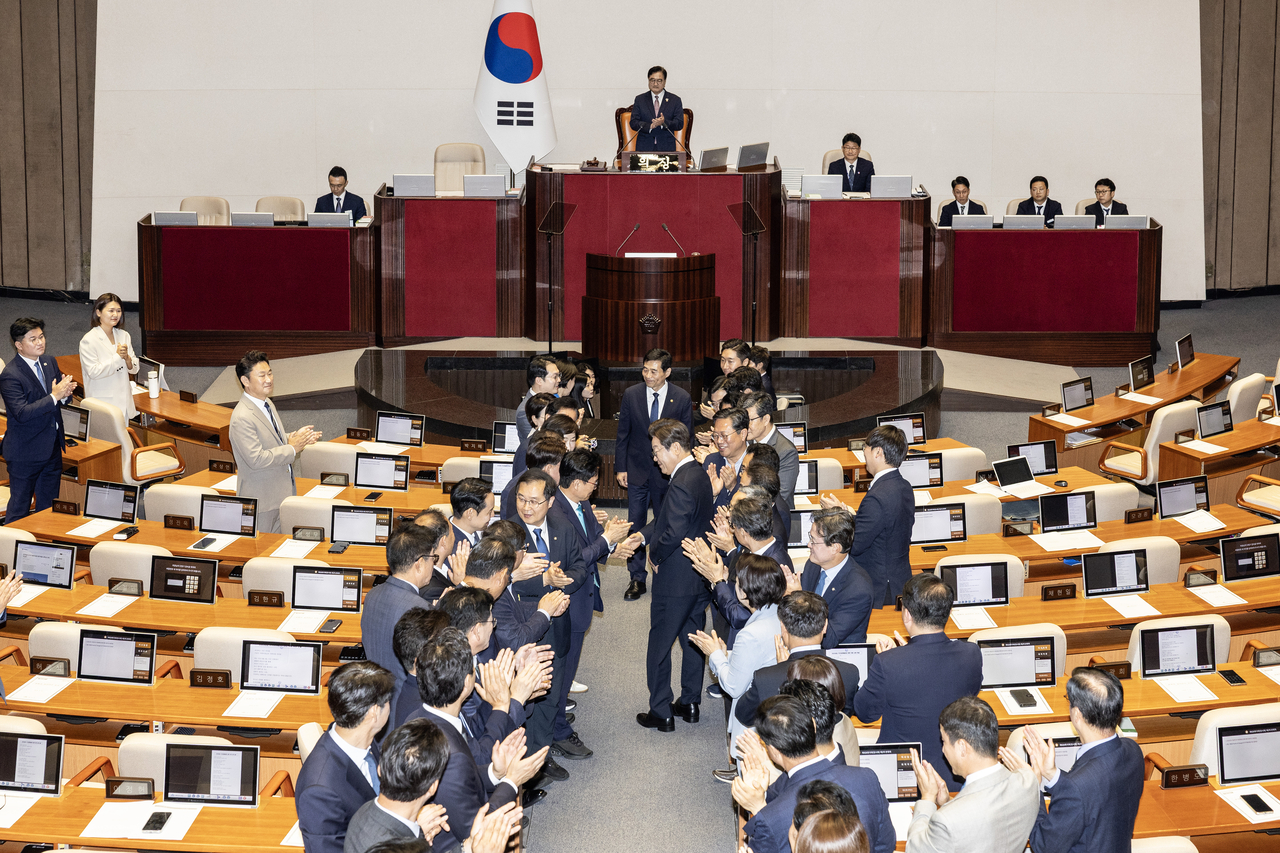 President Lee Jae Myung (center) walks down an aisle in the main hall of the National Assembly on Thursday while shaking hands with ruling Democratic Party of Korea lawmakers. (Yonhap)