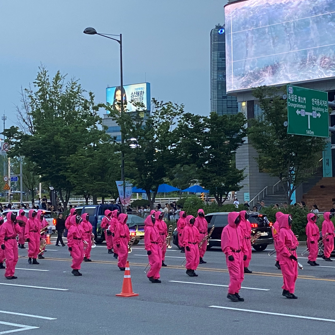 Squid Game parade actors in pink guard suits marching on Sejong-daero in Seoul, a key K-drama filming location stop
