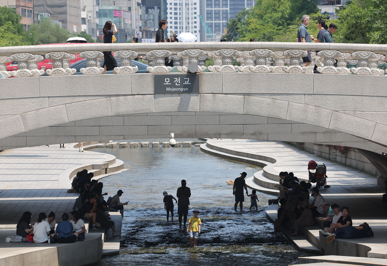 Visitors to Cheonggyecheon relax in the shade beneath the Mojeon Bridge on June 23. (Yonhap)