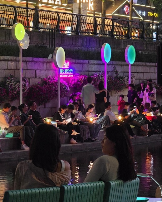 Visitors relax with books along the Cheonggyecheon stream at the outdoor library "Clear Stream for Reading Books," on June 5. (Seoul Metropolitan Government)
