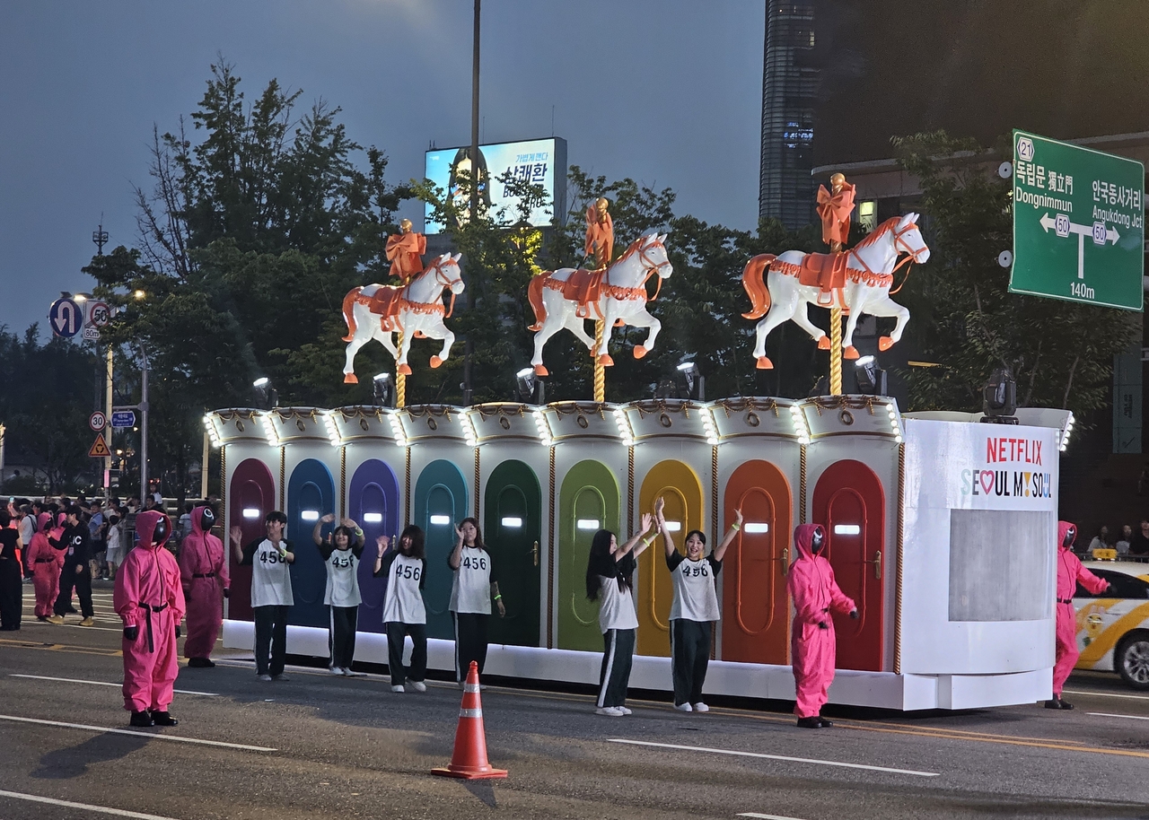 Actors dressed in "Squid Game" player costumes parade alongside a float depicting the "Round and Round" game from "Squid Game" Season 2 in Seoul on Saturday. (Lee Yoon-seo/The Korea Herald)