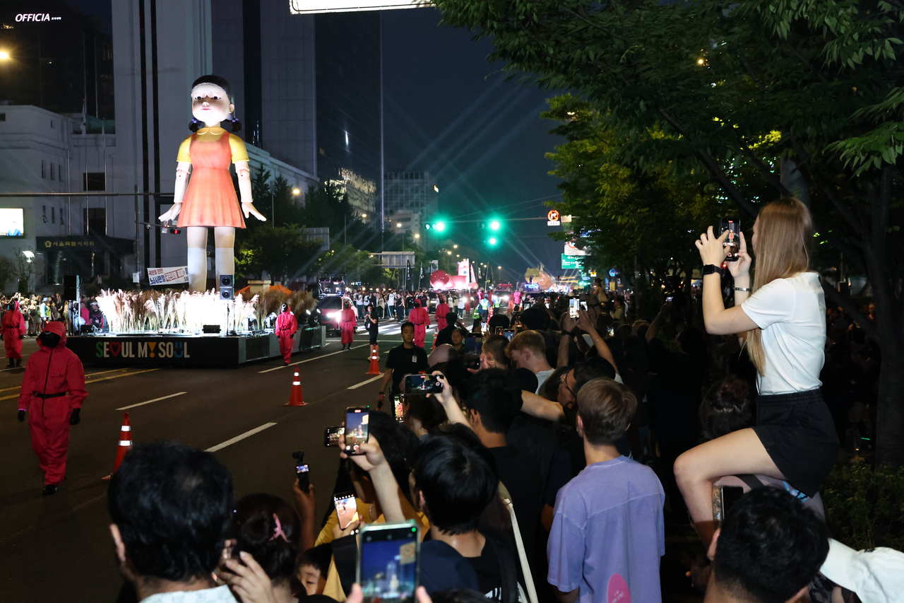 Spectators watch as the doll Young-hee from "Squid Game" is paraded down Sejong-daero during Saturday’s celebration marking the series finale. (Yonhap)