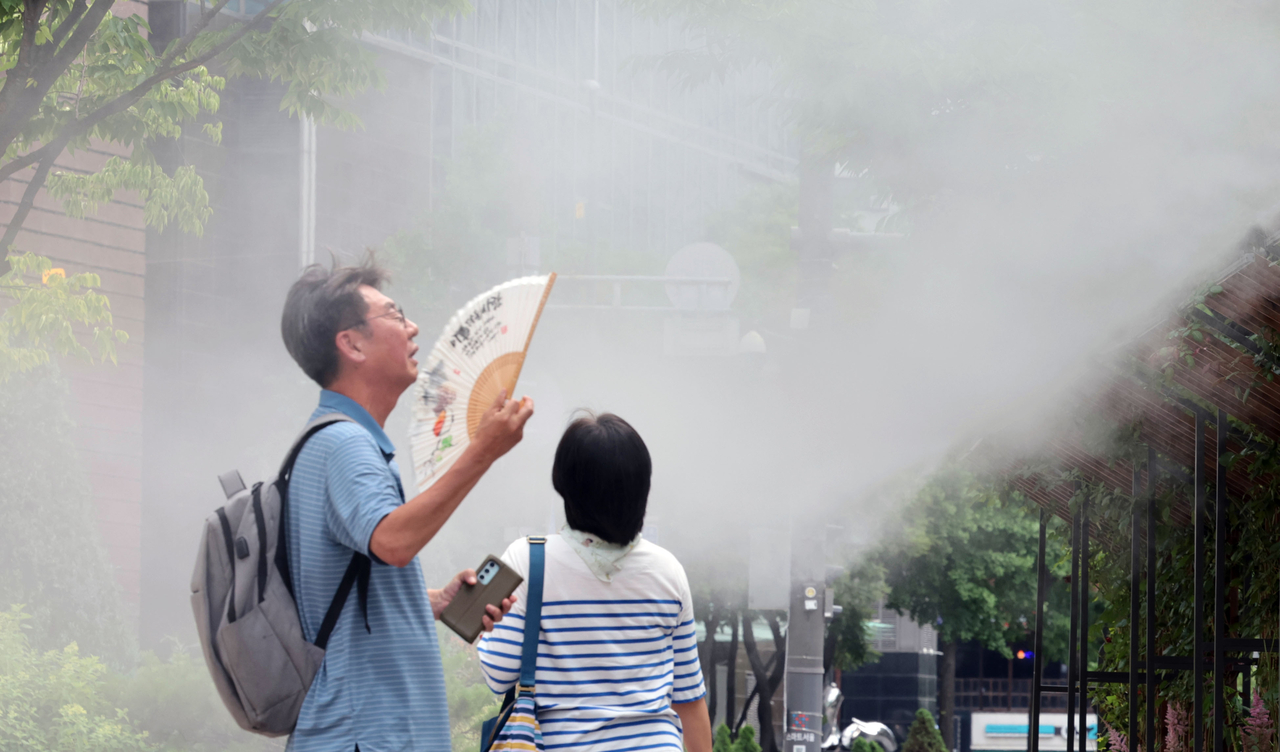 A man fans himself in front of a cooling fog system at Seoul Plaza on Tuesday. (Yonhap)