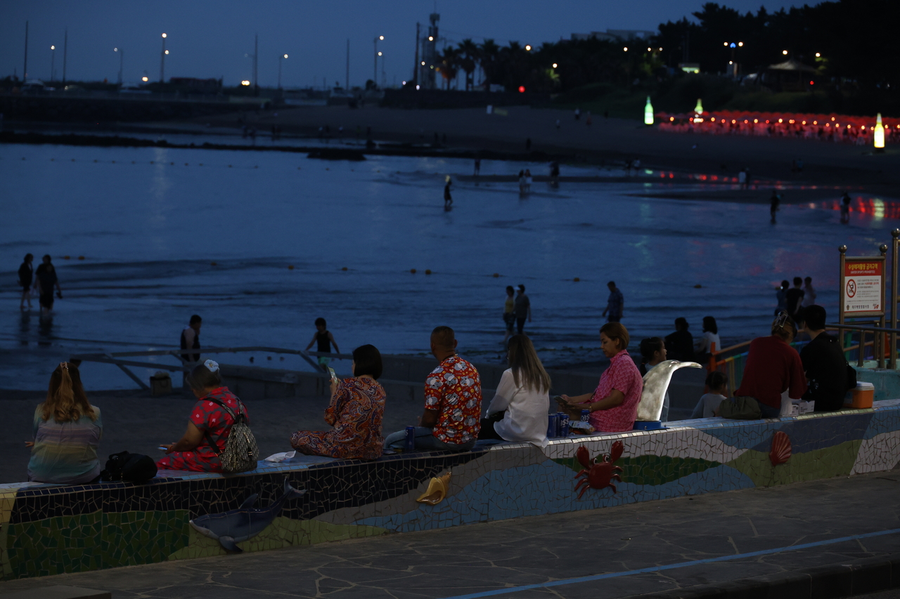 People dip their feet in the sea to cool off on the coast of Jeju Island on Tuesday. (Yonhap)
