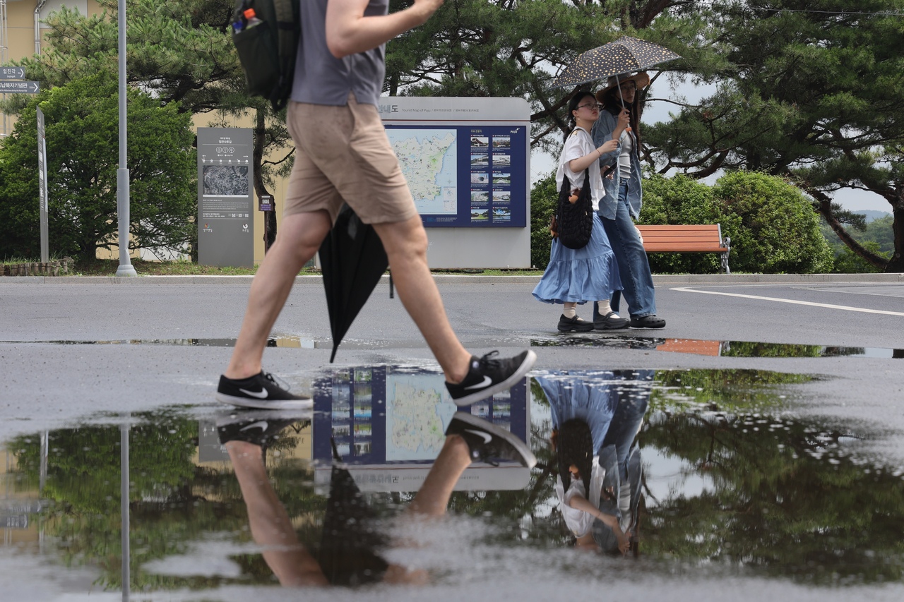 Tourists at Imjingak in Paju, Gyeonggi Province, walk through puddles following monsoon rain, while shielding themselves from the sunlight on Tuesday. (Yonhap)
