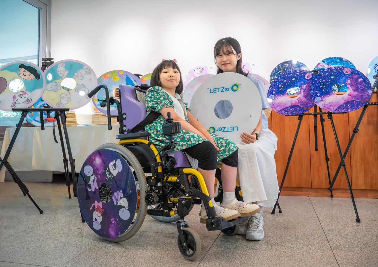A child (left) who participated in LG Chem’s social contribution program shows her custom-decorated spoke guard, made from recycled plastic, alongside a designer. (LG Chem)