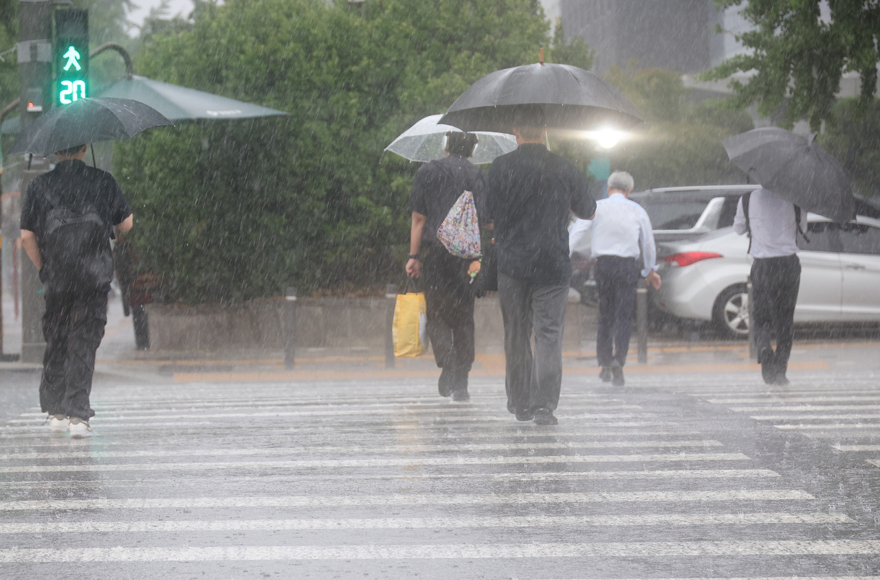 People cross a crosswalk with umbrellas near the National Assembly in Seoul as a sudden downpour hits the area during the evening commute hours on July 8, 2025. (Yonhap)