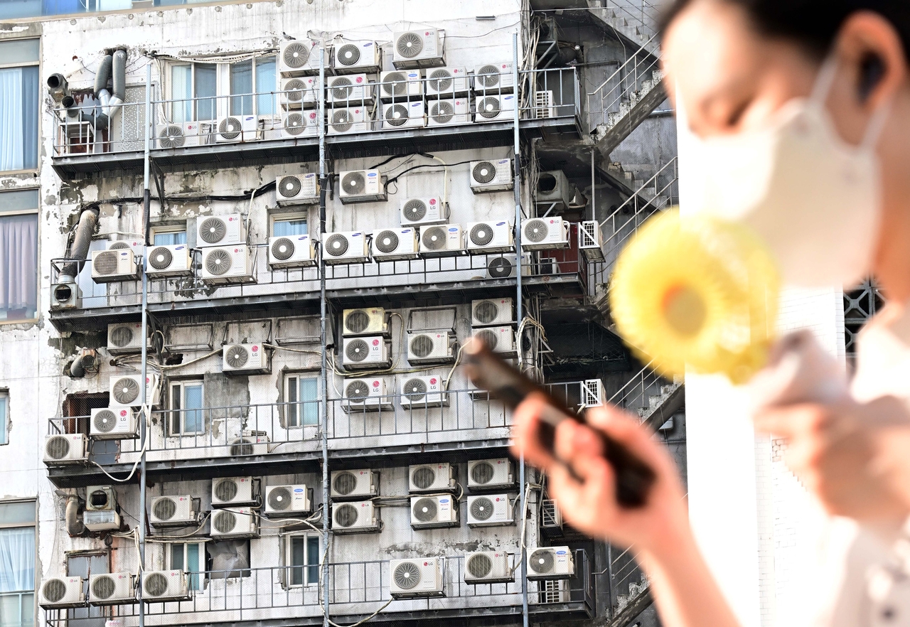 Amid a relentless heat wave, a person walks past a row of air conditioner outdoor units mounted on the exterior wall of a building near Namdaemun in Jung-gu, central Seoul, Wednesday. (Lee Sang-sub/The Korea Herald)