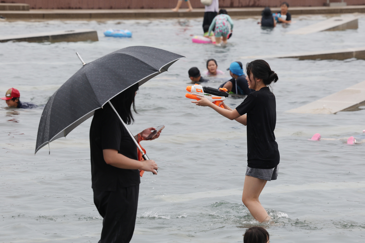 A student plays in the water while holding an umbrella at Yeouido Water Light Square in Seoul on Sunday. (Yonhap)