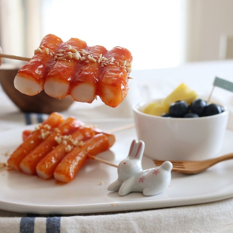 Brushing homemade gochujang ketchup and honey glaze sauce onto grilled rice cake skewers tteokkochi, the key finishing step in the Korean street food recipe