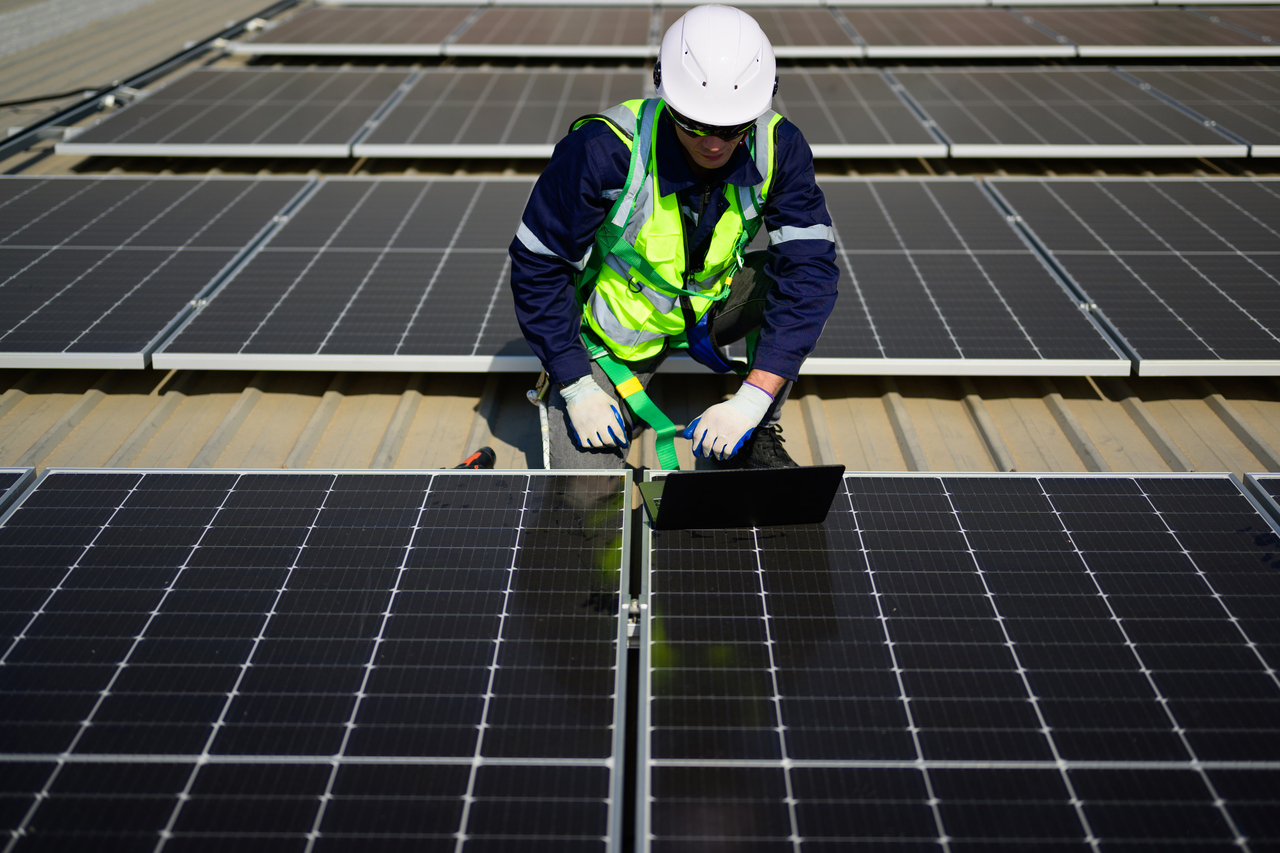 A technician uses a laptop to check and operate the system on the rooftop of a solar cell farm power plant. (123rf)