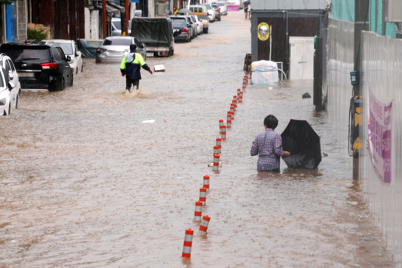 People wade through a flooded street in Gwangju on Thursday. (Yonhap)