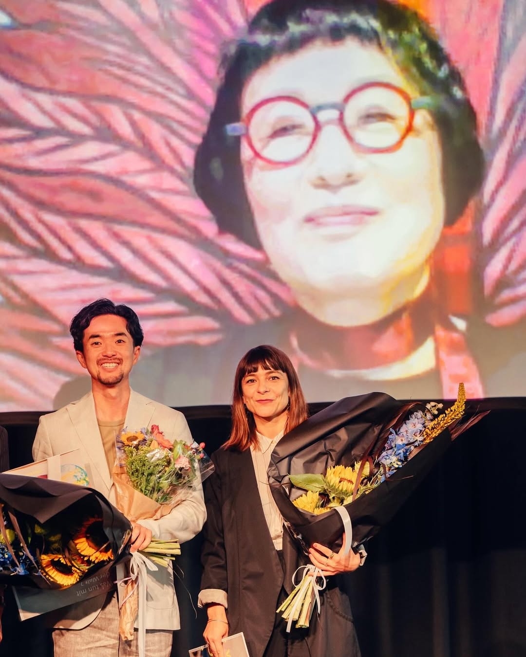 Translators Park Sool (left) and Uljana Wolf pose for a photo during the award ceremony for the Prize for Contemporary Literatures in Translation. On screen is poet Kim Hye-soon. (Hanna Wiedemann/HKW)