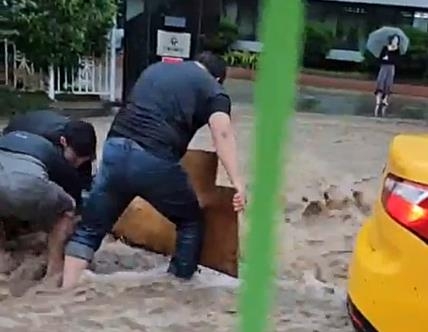 Choi Seung-il and workers at his repair shop help an old man, whose leg was stuck inside a manhole, during a flood in Gwangju on Thursday. (Yonhap)