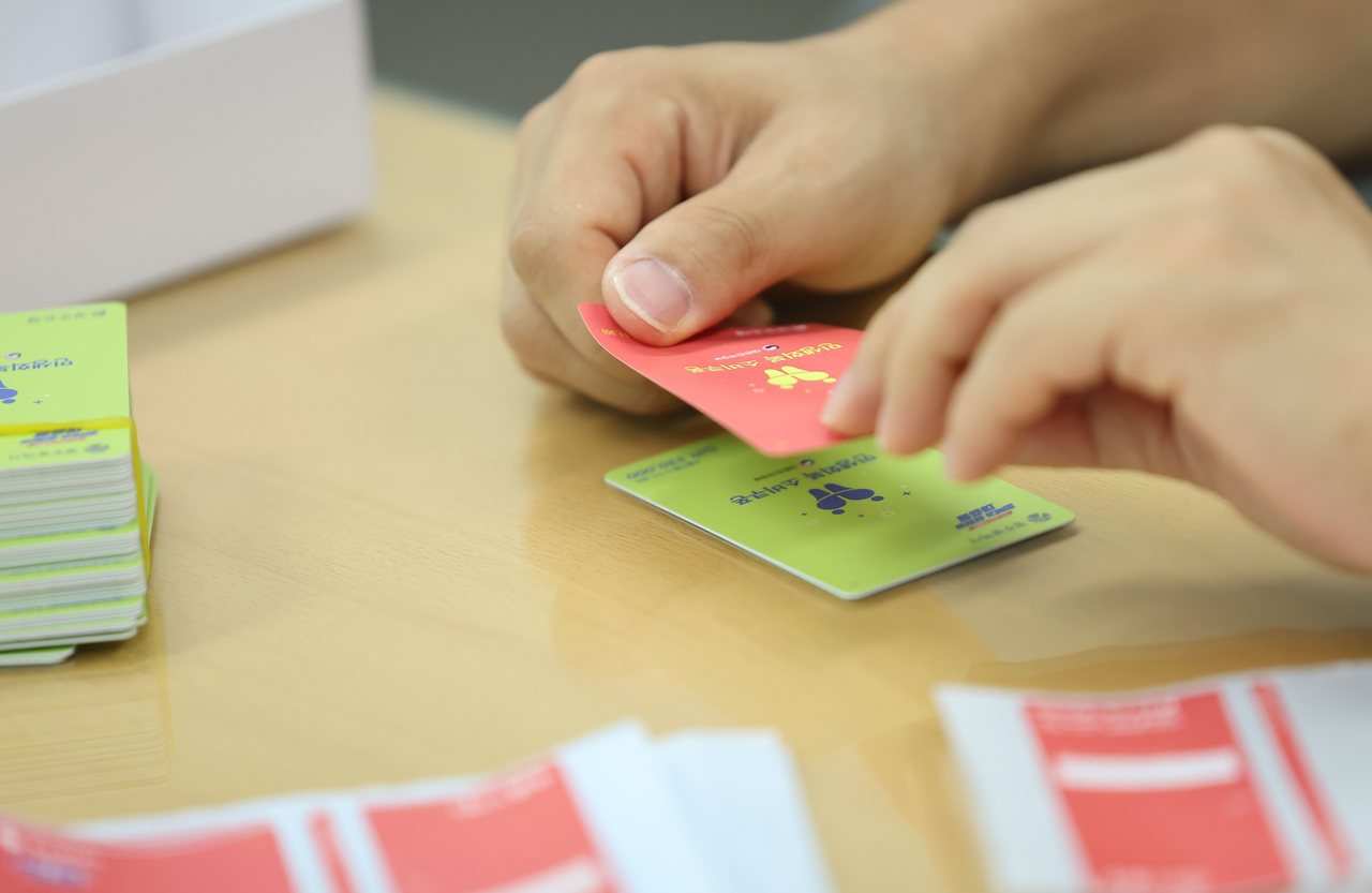 A Gwangju government employee attaches a sticker to cover a green consumer voucher card at an administrative center in Buk-gu, Gwangju, Thursday. The city’s prepaid cards were originally color-coded by income, with green designated for lower-income recipients. (Yonhap)