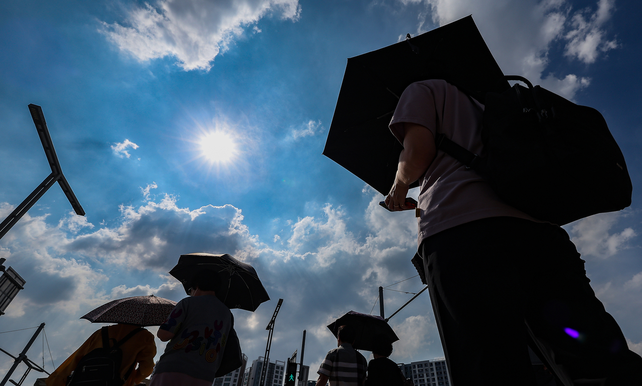 People walk across the plaza outside Dongdaegu Station in Daegu, using parasols to shield themselves from the sun on Wednesday. (Yonhap)