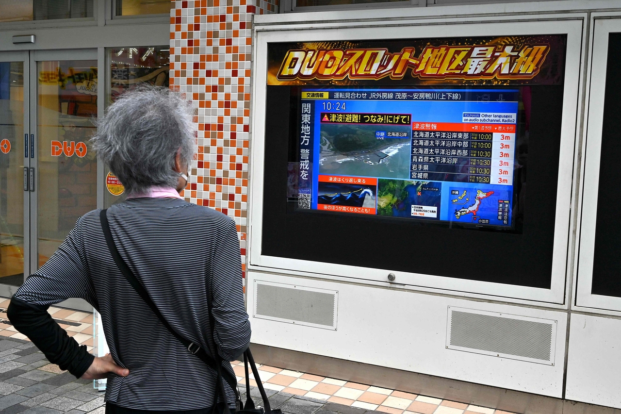 A woman watches a television broadcast of a tsunami warning for much of coastal Japan following a 8.7 magnitude quake in the sea off eastern Russia, outside a gaming shop in central Tokyo on Wednesday. (AFP via Yonhap)