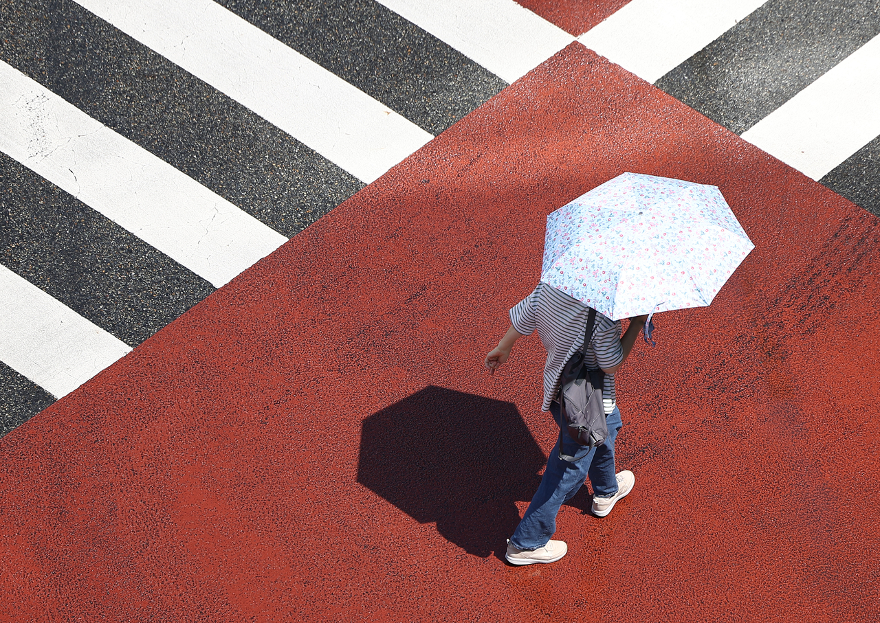 A pedestrian crosses the street with a parasol near Wangsimni Station in Seongdong-gu, eastern Seoul, Tuesday. (Yonhap)