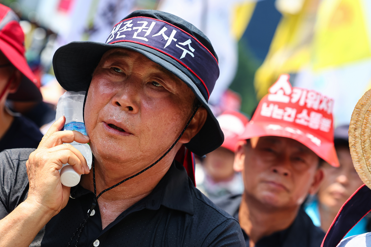 A participant at a farmers' rally against potential agricultural market openings in Yongsan-gu, Seoul, cools off by pressing ice water to his neck on Monday, when Seoul’s daytime temperature soared to 36 degrees Celsius. (Yonhap)