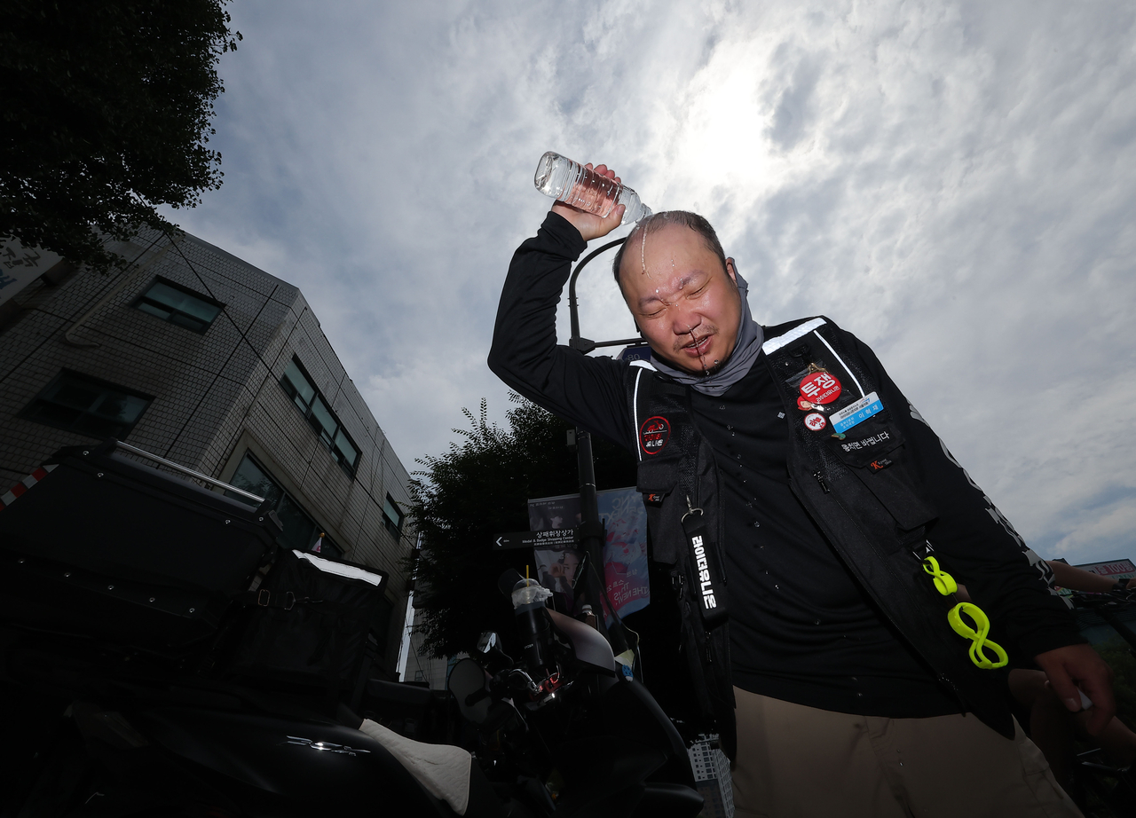 A delivery worker pours bottled water over his head to cool down in Seoul on Wednesday. (Yonhap)