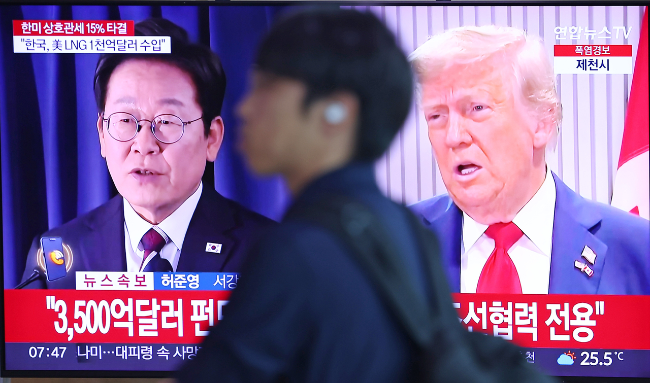 A passerby walks past a TV broadcasting news about the concluded tariff negotiations between South Korea and the United States at Seoul Station’s main concourse on Thursday. (Yonhap)