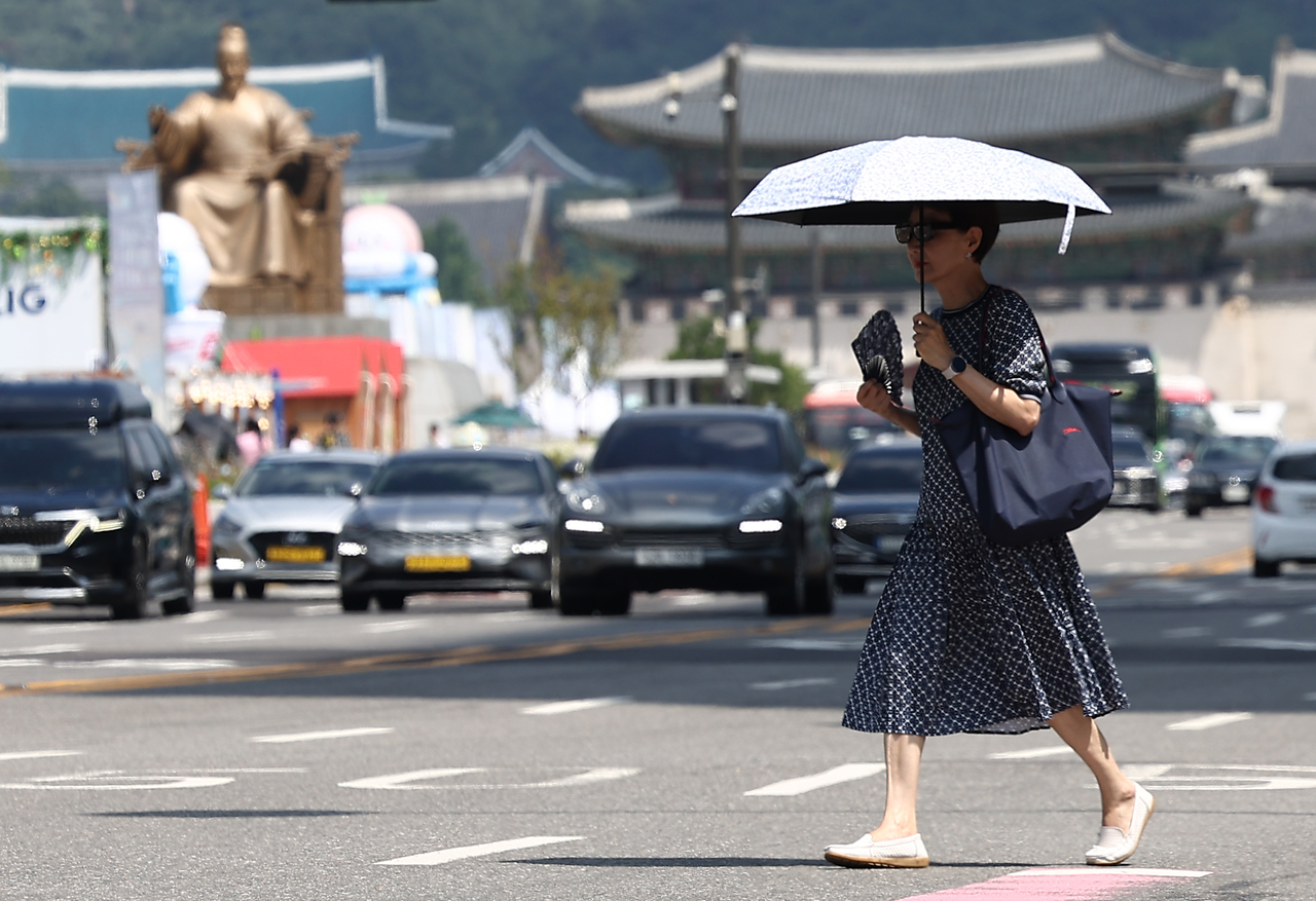 A civilian crosses the street with a parasol near Gwanghwamun Square in Jongno-gu, central Seoul, Tuesday, when a heat wave warning was issued in the city. (Yonhap)