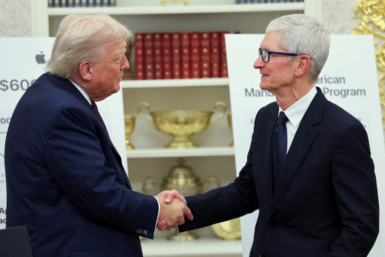 US President Donald Trump (left) and Apple CEO Tim Cook shake hands on the day they present Apple's announcement of a $100 billion investment in US manufacturing, in the Oval Office at the White House in Washington, on Wednesday.   Reuters-Yonhap