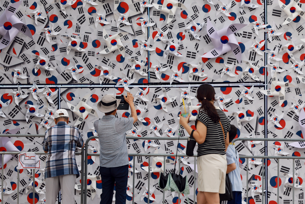 Citizens walk past a wall covered with hundreds of Taegukgi, South Korea’s national flag, set up in front of the Seoul Metropolitan Library in central Seoul on Friday. (Yonhap)
