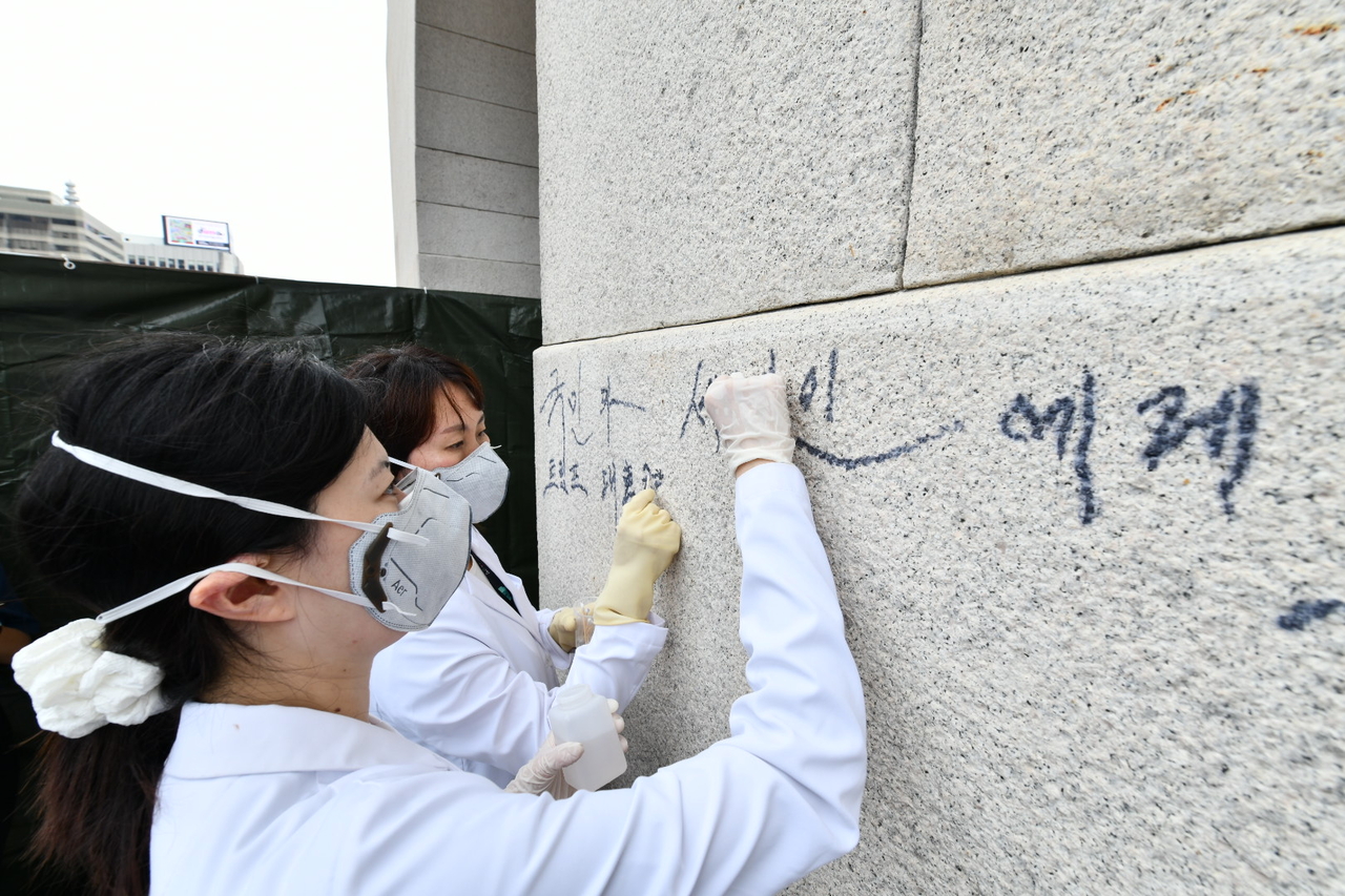 Conservation experts from the National Palace Museum of Korea work to remove graffiti from the stone wall of Gwanghwamun in central Seoul, after a 79-year-old man defaced the historic structure with marker writing on Monday. (Korea Heritage Service)