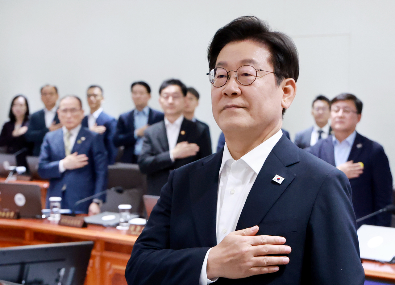 President Lee Jae Myung (front) pays respects to the national flag during an extraordinary Cabinet meeting on Monday. (Yonhap)