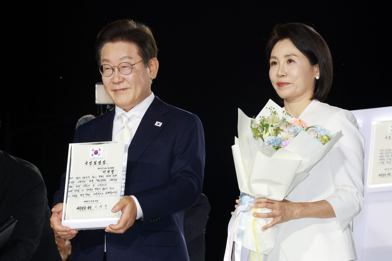 President Lee Jae Myung holds up his letter of appointment, received from the CEO of NCSoft’s artificial intelligence division Lee Yeon-soo, at his inauguration ceremony held at Gwanghwamun Square in Jongno-gu, central Seoul, Friday. First lady Kim Hea Kyung stands next to Lee, holding a bouquet. (Yonhap)