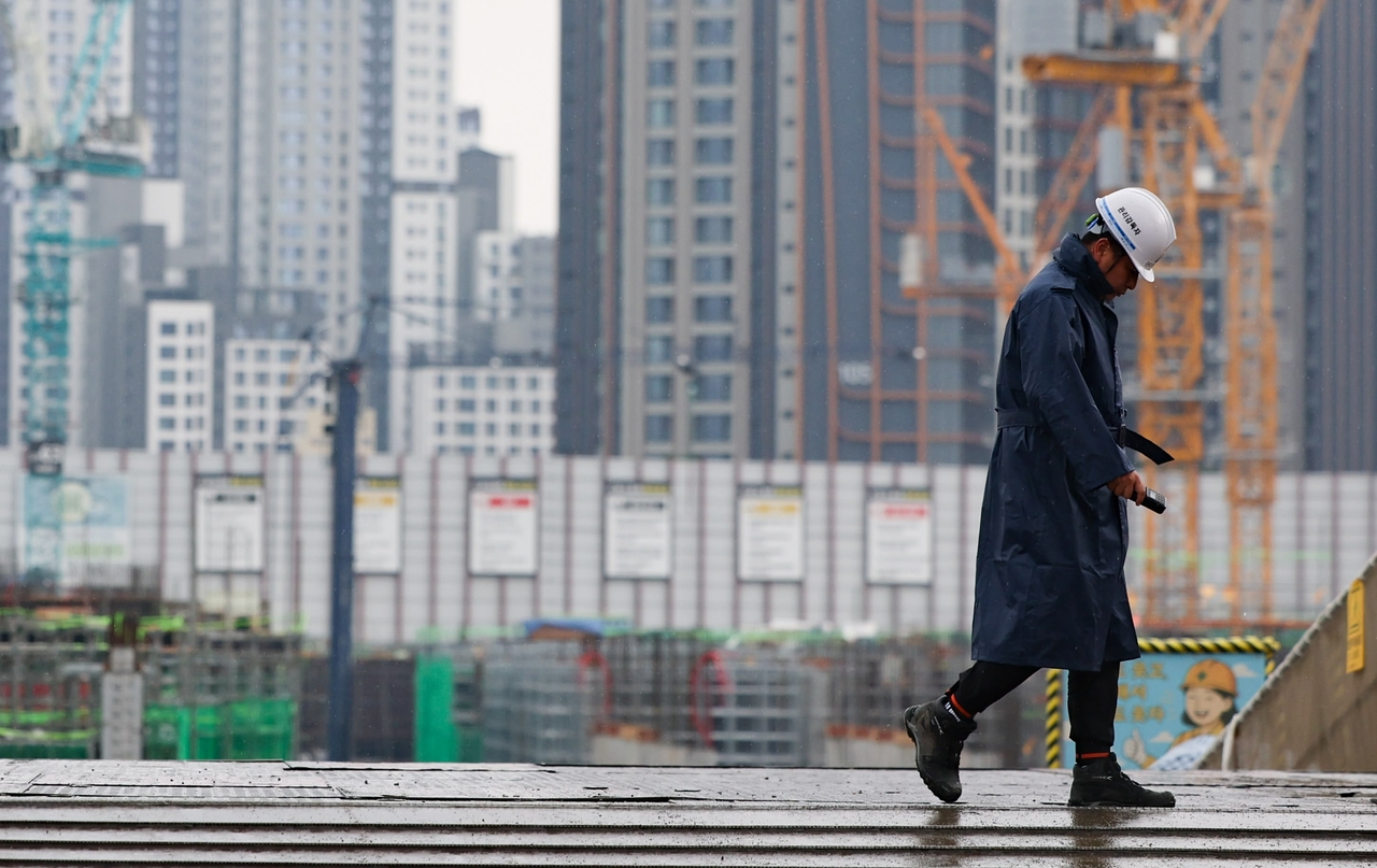 A construction worker crosses a site in Seoul in July with cranes and apartment towers in the distance. The scene is unrelated to the specific cases covered in the article. (Newsis)