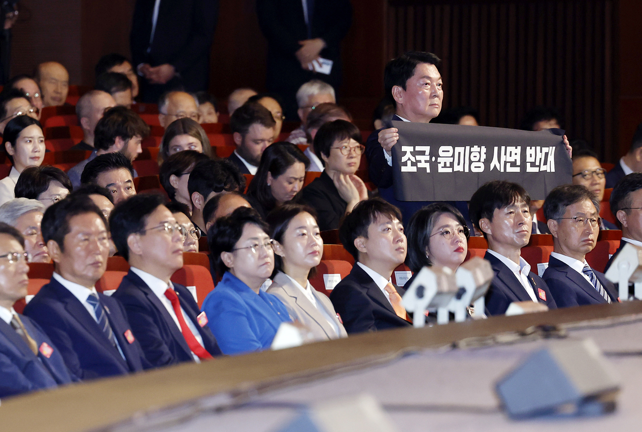 Rep. Ahn Cheol-soo (standing with banner) is seen displaying a sign protesting President Lee Jae Myung's decision to grant a pardon to convicted liberal politicians Cho Kuk and Youn Mee-hyang, during the ceremony to celebrate Liberation Day on Friday. (Pool photo via Yonhap)
