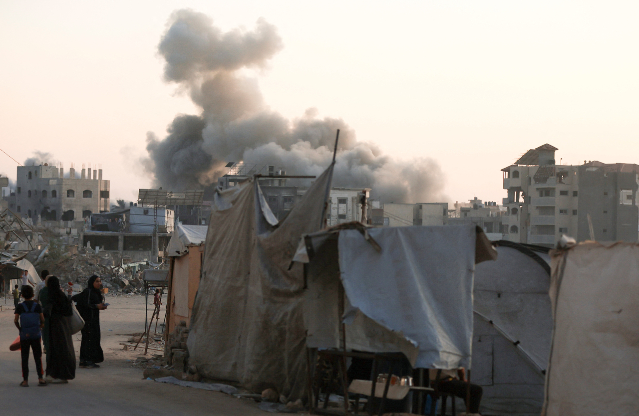Palestinians stand as smoke rises following an Israeli strike in Gaza City on Wednesday.   Reuters-Yonhap